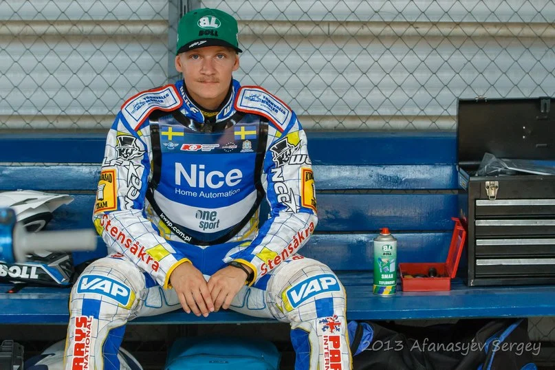 Fredrik Lindgren i svensk förardräkt och grön keps sittande på en bänk i depån 2013